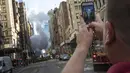 Seorang pria mengambil foto dengan smartphone miliknya di lokasi meledaknya sebuah pipa uap di Fifth Avenue dekat Distrik Flatiron, Manhattan, Kamis (19/7). Ledakan itu meninggalkan kawah besar di jalan. (Drew Angerer/Getty Images/AFP)