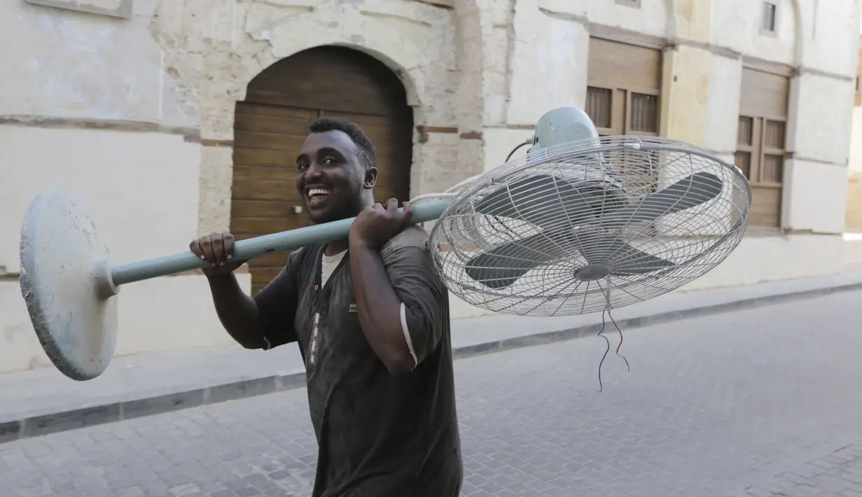 Seorang pekerja Somalia membawa kipas angin tua di Kota Tua Jeddah, Arab Saudi (8/11/2021). Kota Tua Jeddah terletak di pantai timur Laut Merah. Kota ini konon telah berumur 3.000 tahun. (AP Photo/Amr Nabil)