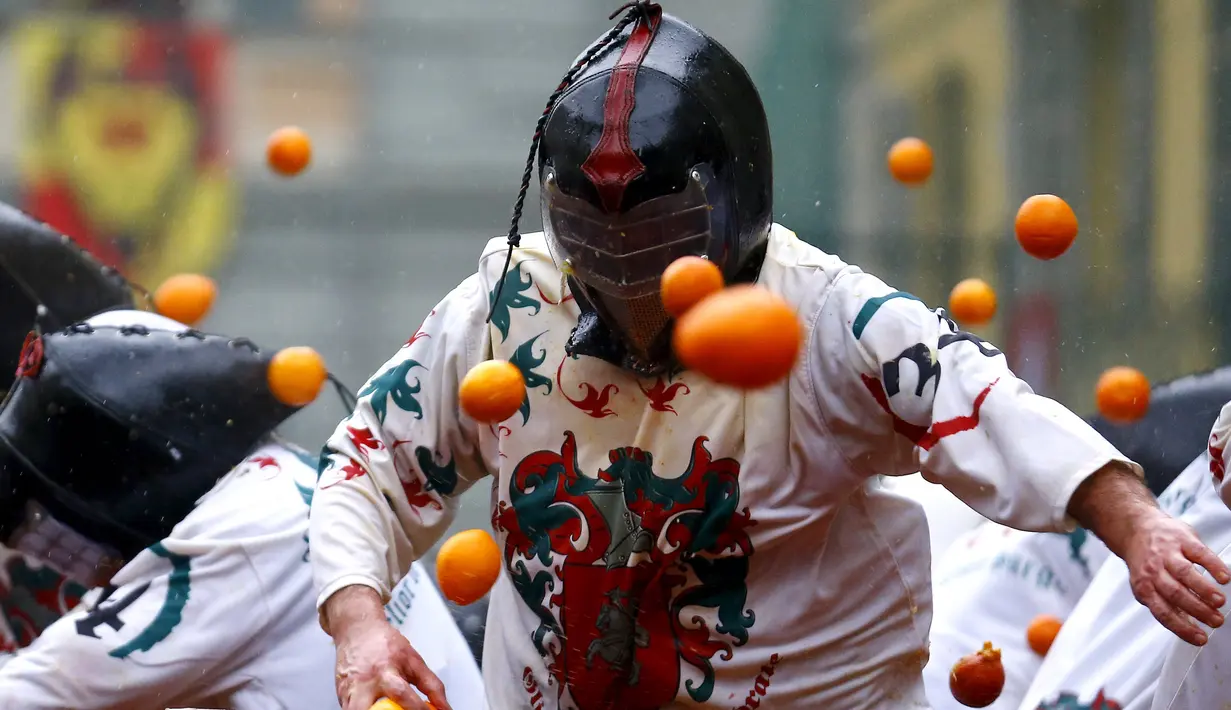Peserta ikut ambil bagian dalam perang-perangan dengan jeruk selama karnaval di kota Ivrea, Italia, Minggu (7/2). Peserta yang dibagi menjadi dua tim ini saling melempar jeruk menggunakan kostum dan aksesoris lengkap. (REUTERS/Stefano Rellandini)