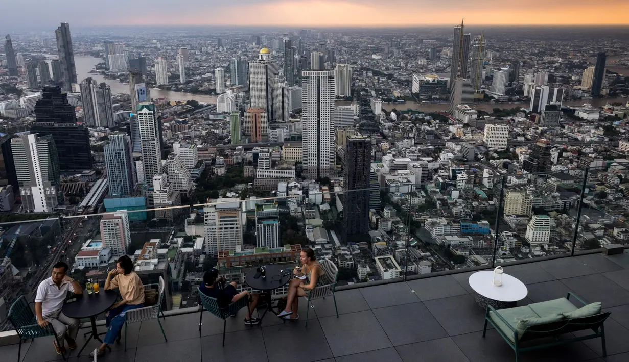 Orang-orang duduk di depan cakrawala Bangkok di dek observasi gedung pencakar langit King Power Mahanakhon pada 25 Oktober 2021. Dek observasi ini menyediakan pemandangan Bangkok tidak hanya 180 derajat, melainkan 360 derajat. (Jack TAYLOR / AFP)