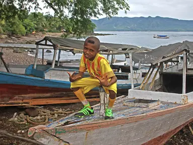 Seorang Anak duduk diatas perahu dengan jersey Barcelona siap untuk bermain sepak bola di Alor, Nusa Tenggara Timur. (Bola.com/Nicklas Hanoatubun)