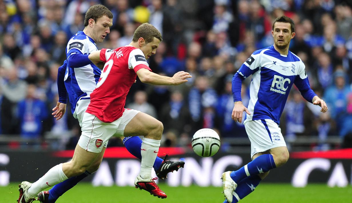 Gelandang Arsenal, Jack Wilshere (tengah) menggiring bola di antara dua pemain Birmingham City pada laga final Piala Liga Inggris 2010/2011 di Wembley Stadium, London (27/2/2011). Jack Wilshere yang belum lama pensiun sebagai pemain pada Juli 2022 bersama klub Denmark, Aarhus GF tercatat pernah berseragam Arsenal selama 10 musim mulai 2008/209 hingga 2017/2018. Gelar PFA Young Player of the Year diraihnya di musim ketiganya pada 2010/2011. (AFP/Glyn Kirk)