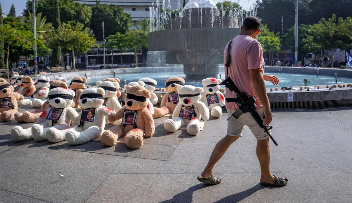 Seorang tentara Israel yang sedang tidak bertugas berjalan melewati instalasi boneka beruang raksasa dengan mata tertutup dan dihiasi foto warga Israel yang ditawan di Gaza di Tel Aviv, Israel, Rabu (25/10/2023). Instalasi tersebut dimaksudkan untuk menarik perhatian lebih dari 200 orang yang diculik oleh militan Hamas dalam serangan lintas batas pada 7 Oktober 2023. (AP Photo/Oded Balilty)