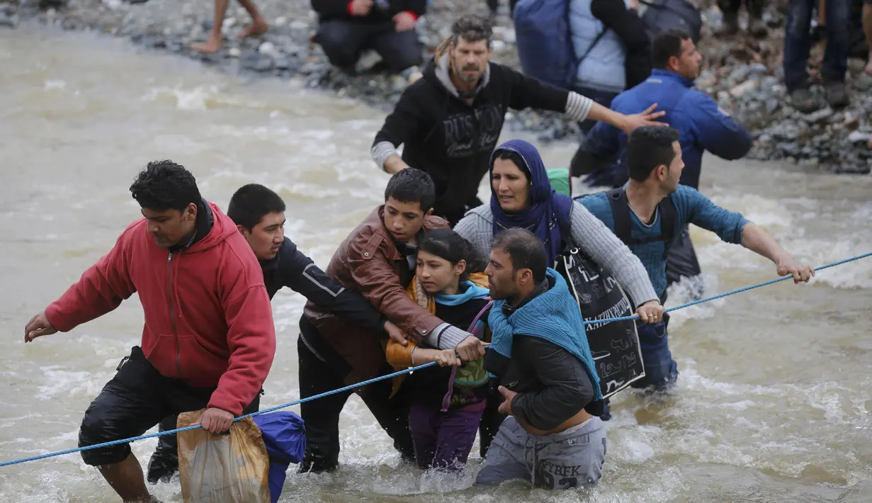 Ribuan migran menyeberangi sungai dengan berpegangan pada seutas tali di perbatasan Yunani-Makedonia, Idomeni, Yunani (14/3/2016). Lebih dari 1.000 migran nekat menembus sungai untuk mencari jalan keluar perbatasan. (Reuters/Stoyan Nenov)