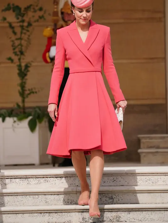 Kate Middleton, Duchess of Cambridge dari Inggris turun dari tangga saat menghadiri Pesta Taman Kerajaan di Istana Buckingham di London (18/5/2022). Kate Middleton memilih gaun mantel Emilia Wickstead versi koral yang telah ia kenakan pada beberapa kesempatan sebelumnya. (AFP/Pool/Dominic Lipinski)