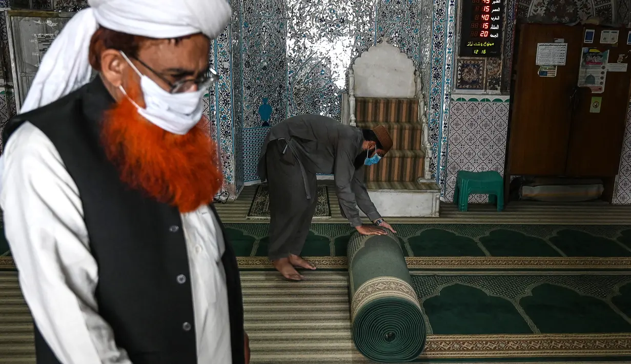 Umat Muslim menggulung karpet sajadah dari aula utama masjid menyusul pembatasan baru pemerintah baru menjelang bulan suci Ramadan di Rawalpindi, Pakistan, Senin (5/4/2021). Warga di atas 50 tahun dan mereka yang menderita sakit harus menghindari datang ke masjid. (Aamir QURESHI/AFP)