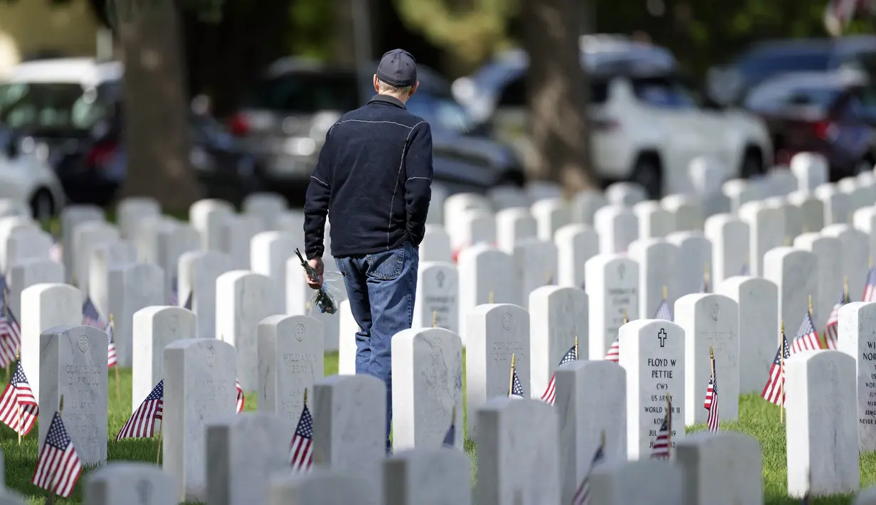Seorang pria membawa karangan bunga melewati deretan batu nisan di Pemakaman Nasional Fort Logan, Sheridan, Colorado, Amerika Serikat, 30 Mei 2022. (AP Photo/David Zalubowski)