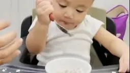 Rayyanza, diberi makan nasi dengan sup daging. Tak ingin disuapi, ia pun berusaha untuk menyantapnya dengan sendok tapi gagal. (Foto: Instagram/@raffinagita1717)