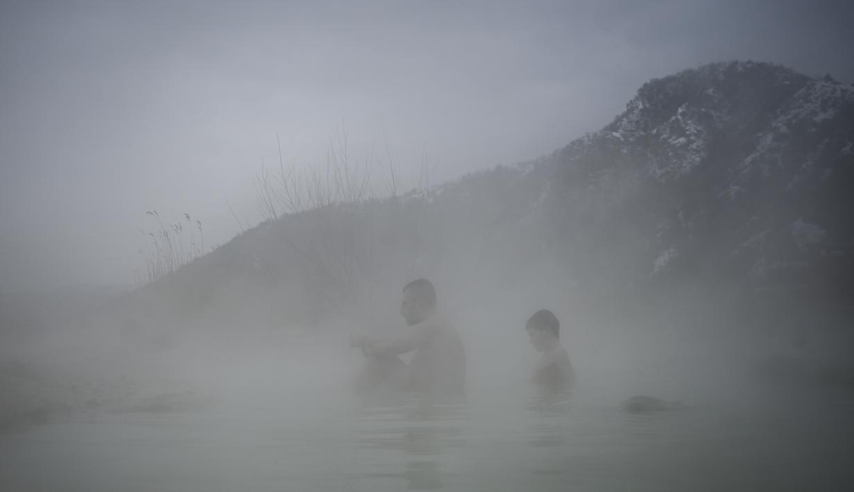 Orang-orang menikmati air panas di mata air mineral alami pada hari musim dingin di dekat desa Rupite, Bulgaria (2/2/2022). Penduduk setempat percaya bahwa air mineral menyembuhkan banyak penyakit dan gangguan. (AFP/Nikolay Doychinov)