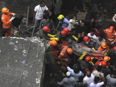 Petugas membawa korban yang selamat dari puing-puing bangunan tempat tinggal tiga lantai yang runtuh di Bhiwandi, India, Senin (21/9/2020). Sepuluh orang tewas dan sekitar 25 lainnya dikhawatirkan masih terjebak setelah bangunan itu runtuh sebelum fajar saat para penghuni terlelap tidur. (AFP)