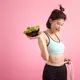 Seorang perempuan sedang mengukur lingkar tubuhnya sambil memegang semangkuk salad (Foto Dok: Freepik/jcomp).
