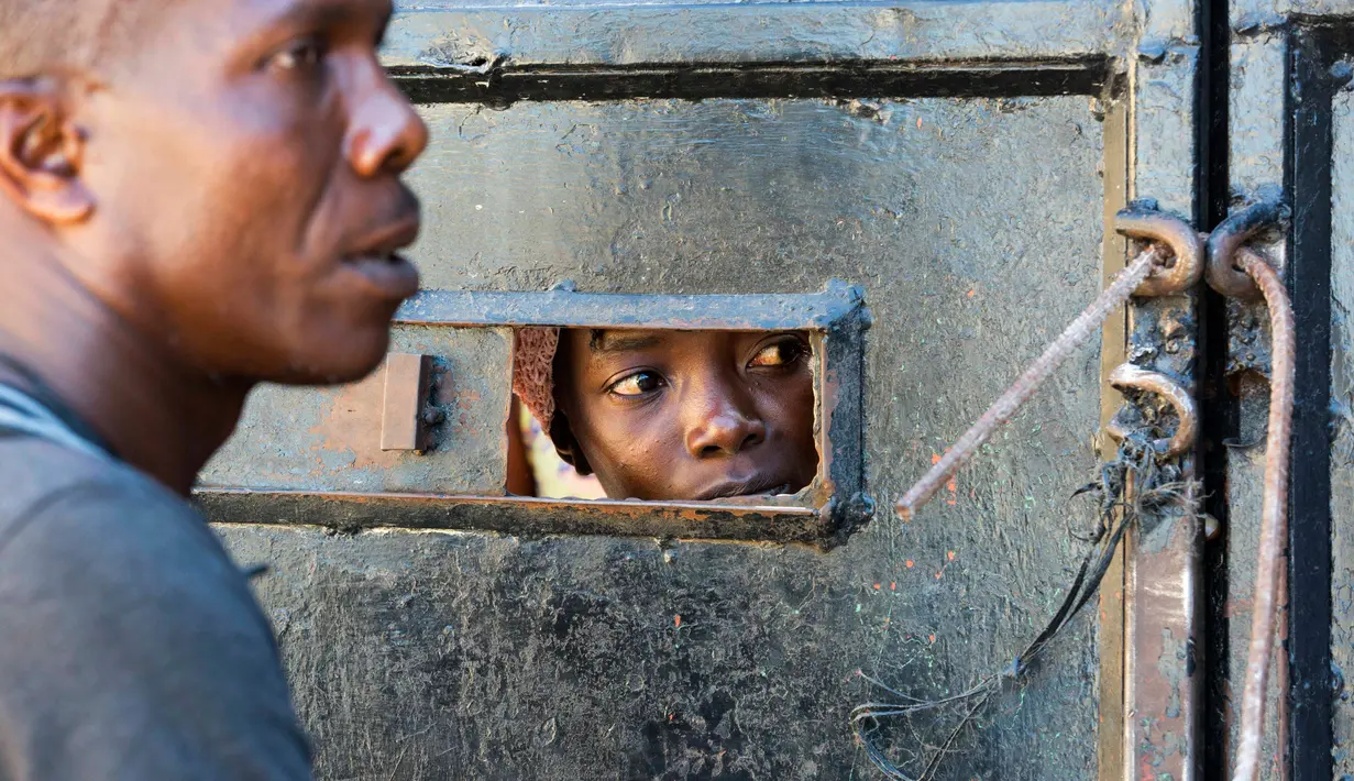 Ibu dari seorang anak yang tinggal di Panti Asuhan Church of Bible Understanding melihat melalui celah kecil di pintu masuk ketika mencari tahu kondisi setelah kebakaran di pinggiran Port-au-Prince di ibu kota Haiti, Jumat (14/2/2020). Lima belas anak tewas dalam kebakaran. (AP/Dieu Nalio Chery)