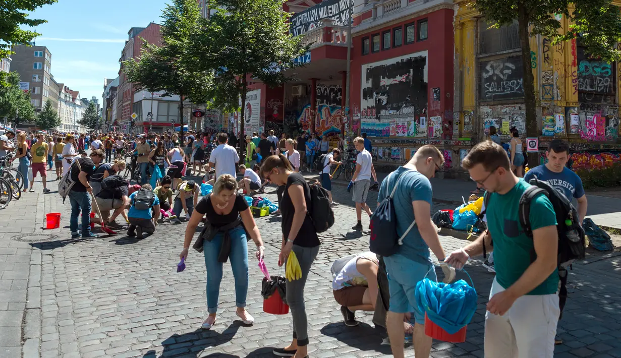 Sejumlah orang membersihkan jalanan di sebuah perumahan setelah aksi protes KTT G20 di Hamburg, Jerman, Minggu (9/7). Dalam aksi tersebut, demonstran nekat membakar mobil, memecahkan kaca jendela dan menjarah sejumlah toko. (Christophe Gateau/dpa/AFP)