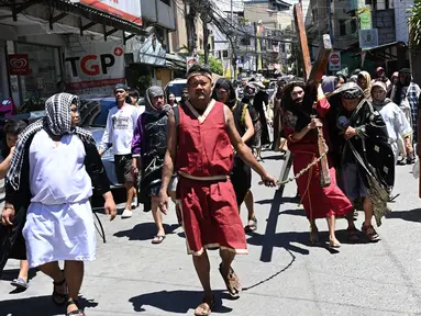 Seorang aktor yang berperan dalam sebuah drama jalanan sebagai Yesus membawa salib kayu saat peragaan penderitaan dan penyaliban pada Pekan Suci di Manila pada 28 Maret 2024. (Ted ALJIBE/AFP)