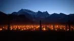 Pemandangan saat ratusan lilin dinyalakan di kebun anggur dengan latar belakang pegunungan es di Flaesch, Swiss (22/3). Sekitar dua ratus lilin anti-embun per hektar dinyalakan untuk melindungi buah dari dingin. (Gian Ehrenzeller / Keystone via AP)