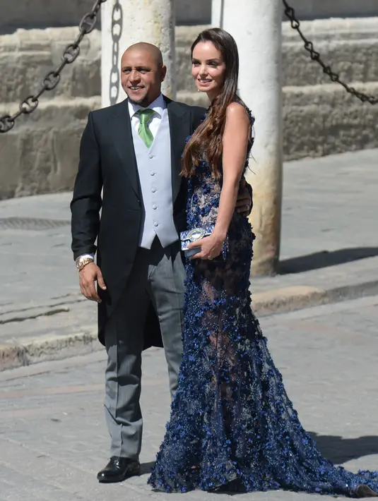 Mantan Pemain Real Madrid Roberto Carlos dan istrinya Mariana Luccon berpose saat tiba di gereja menghadiri upacara pernikahan bek Sergio Ramos dan Pilar Rubio di Katedral Seville, Spanyol (15/6/2019). (AFP Photo/Cristina Quicler)