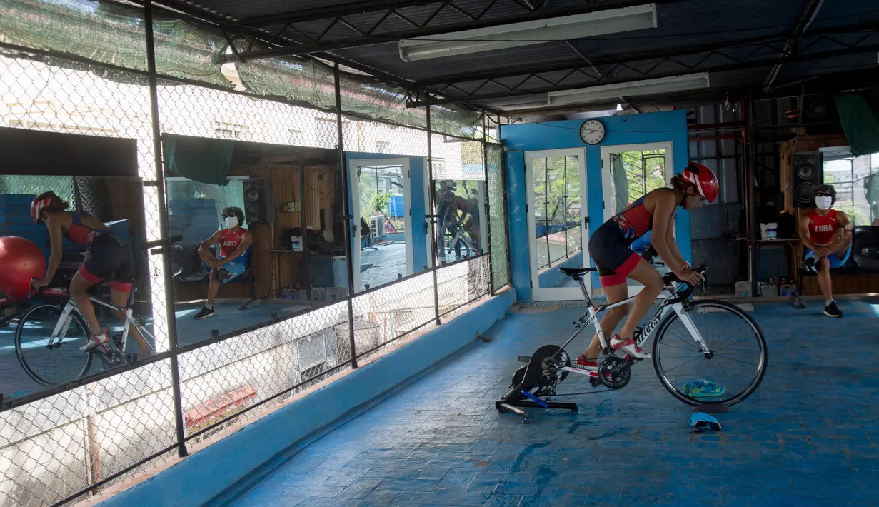Atlet triathlon Kuba, Leslie Amat mengendarai sepedanya, diadaptasi menjadi stasioner, di bawah pengawasan pelatihnya Dioseles Fernandez di teras rumahnya di Havana, Senin (20/4/2020). Atlet Kuba tak bisa berlatih di fasilitas olahraga seperti biasanya selama pademi corona. (AP /Ismael Francisco)