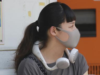 Seorang wanita mengenakan masker wajah untuk membantu melindungi dari penyebaran coronavirus menggunakan kipas angin portabel di lehernya untuk melindungi tubuh dari panas di Tokyo, Rabu, (5/8/2020). (AP Photo/Koji Sasahara)