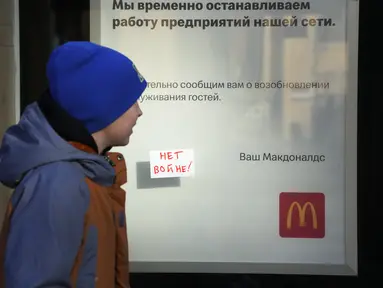 Seorang anak melewati tanda 'No War!' yang menempel di jendela restoran McDonald's dengan pemberitahuan penutupan restoran di St. Petersburg, Rusia, Selasa (15/3/2022). Gerai makanan siap saji McDonald's resmi menutup 850 gerainya yang beroperasi di Rusia pada 14 Maret 2022. (AP Photo)