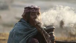 Seorang wanita nomaden merokok hukka, atau gelembung hubble, saat kelompok mereka berhenti sementara di jalan raya Jammu-Srinagar di Nagrota, di pinggiran Jammu, India, Selasa (9/11/2021). Anggota suku tersebut pindah dari perbukitan untuk menghindari musim dingin. (AP Photo/Channi Anand)