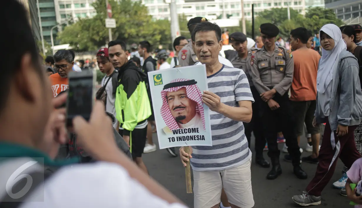 Seorang pria berfoto sambil memegang poster bergambar Raja Salman, saat acara pawai suka cita menyambut kedatangan Raja Arab Saudi Salman bin Abdulaziz di kawasan Car Free Day, Bundaran HI, Jakarta, Minggu (26/2). (Liputan6.com/Faizal Fanani)