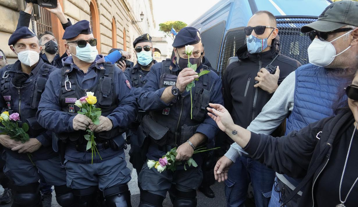 Petugas polisi memegang bunga yang diberikan demonstran selama aksi protes di Circus Maximus Roma, Jumat (15/10/2021). Protes tersebut karena aturan yang mengharuskan seluruh pekerja di Italia menunjukkan kartu kesehatan covid-19 untuk memasuki tempat kerja mereka. (AP Photo/Gregorio Borgia)