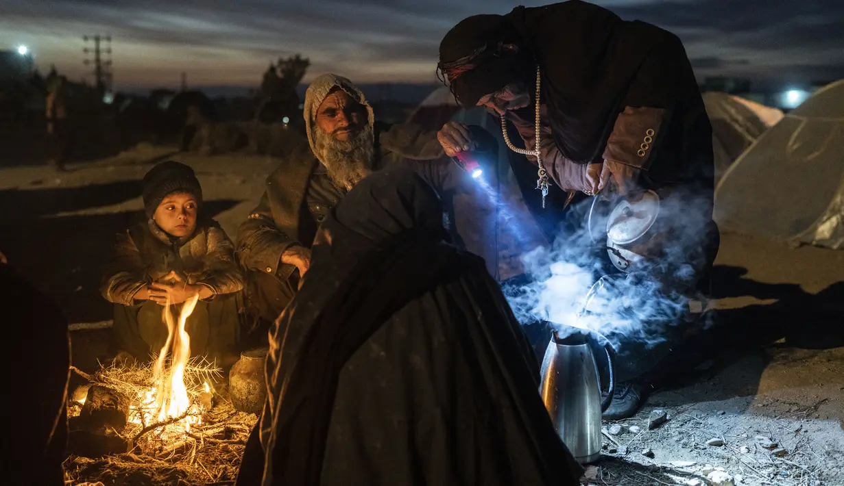Sebuah keluarga menyiapkan teh di luar kantor Direktorat Bencana tempat mereka berkemah, di Herat, Afghanistan (29/11/2021). Sekitar 2000 pengungsi meninggalkan desa Allahyar di provinsi Ghor karena kekeringan dan mencari bantuan dari pemerintah daerah di Herat. (AP Photo/Petros Giannakouris)