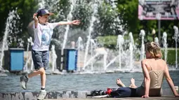Orang-orang menikmati musim semi yang panas dengan bermain dekat air mancur di Moskow, Rusia, Selasa (18/5/2021). Suhu di Moskow telah mencapai 31 derajat Celcius. (Alexander NEMENOV/AFP)