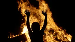 Warga menari di dekat kobaran api saat mengikuti tradisi malam San Juan's (Saint John) di Gijon, Spanyol, (24/6). Malam San Juan adalah upacara penyucian dimana warga membakar sejumlah benda yang sudah tidak diinginkan. (REUTERS/Eloy Alonso)