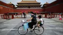 <p>Seorang perempuan mengendarai sepedanya dengan seorang anak duduk di kursi belakang melewati Kota Terlarang di Beijing, China, Selasa (7/6/2022). Pemerintah melonggarkan beberapa pembatasan Covid-19 dengan sebagian besar museum gedung bioskop, dan pusat kebugaran diizinkan beroperasi hingga 75 persen dari kapasitas. (WANG Zhao / AFP)</p>