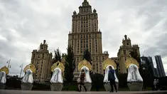 Orang-orang berjalan melewati "benda seni Matryoshki", tujuh boneka bersarang tradisional Rusia "matryoshka" dengan hiasan kepala "kokoshnik", di depan gedung pencakar langit era Soviet "Ukraina" hotel di pusat kota Moskow (9/9/2021).  (AFP/Kirill Kudryavtsev)