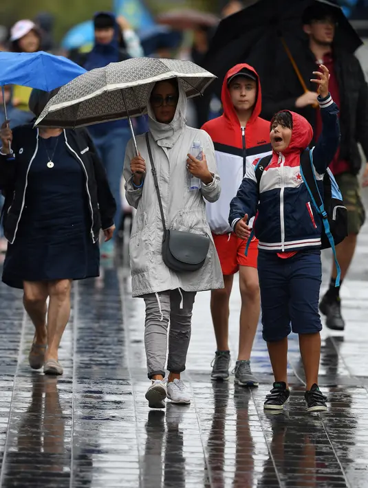 Penonton berjalan di tengah hujan pada hari pertama turnamen tenis Australia Terbuka di Melbourne, Senin (20/1/2020). Pertandingan Roger Federer melawan Steve Johnson sempat terhenti akibat hujan deras yang mengguyur Rod Laver Arena.  (AFP Photo/Greg Wood)