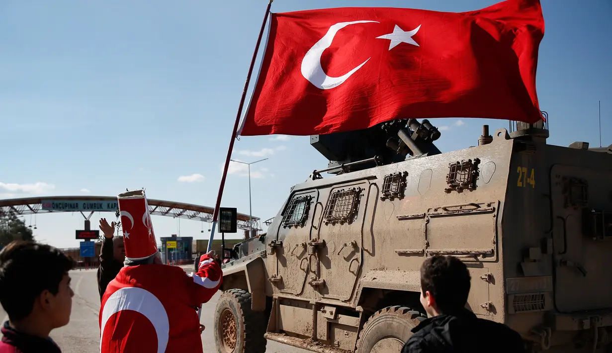 Isikli Tosun Baba (60) melambaikan bendera saat pasukan Turki bergerak melewatinya di Oncupinar, Kilis, Turki, Minggu (28/1). Aksi itu dilakukan untuk mendukung serangan pasukan Turki ke kantung Kurdi di Afrin, Suriah. (AP Photo/Lefteris Pitarakis)
