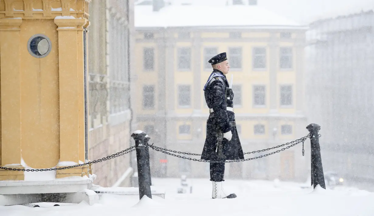 Seorang penjaga kerajaan berdiri saat salju turun di luar Royal Castle di Stockholm, Swedia (28/1/2021). Salju turun sekitar lima hingga sepuluh sentimeter diperkirakan akan turun - atau bahkan hingga 15 sentimeter di bagian pesisir di wilayah timur laut Uppsala. (Henrik Montgomery/TT via AP)