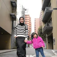 Dwi Handayani menggandeng sang buah hati yang berpose dengan manis. Dwi Handayani mengenakan sweater bergaris hitam-putih dan rok panjang berwarna hitam dengan detail kerut di sisi kanan-kiri. Sang buah hati mengenakan wool jacket berwarna magenta dan celana jeans yang ditutup dengan high boots putih. Foto: Instagram.