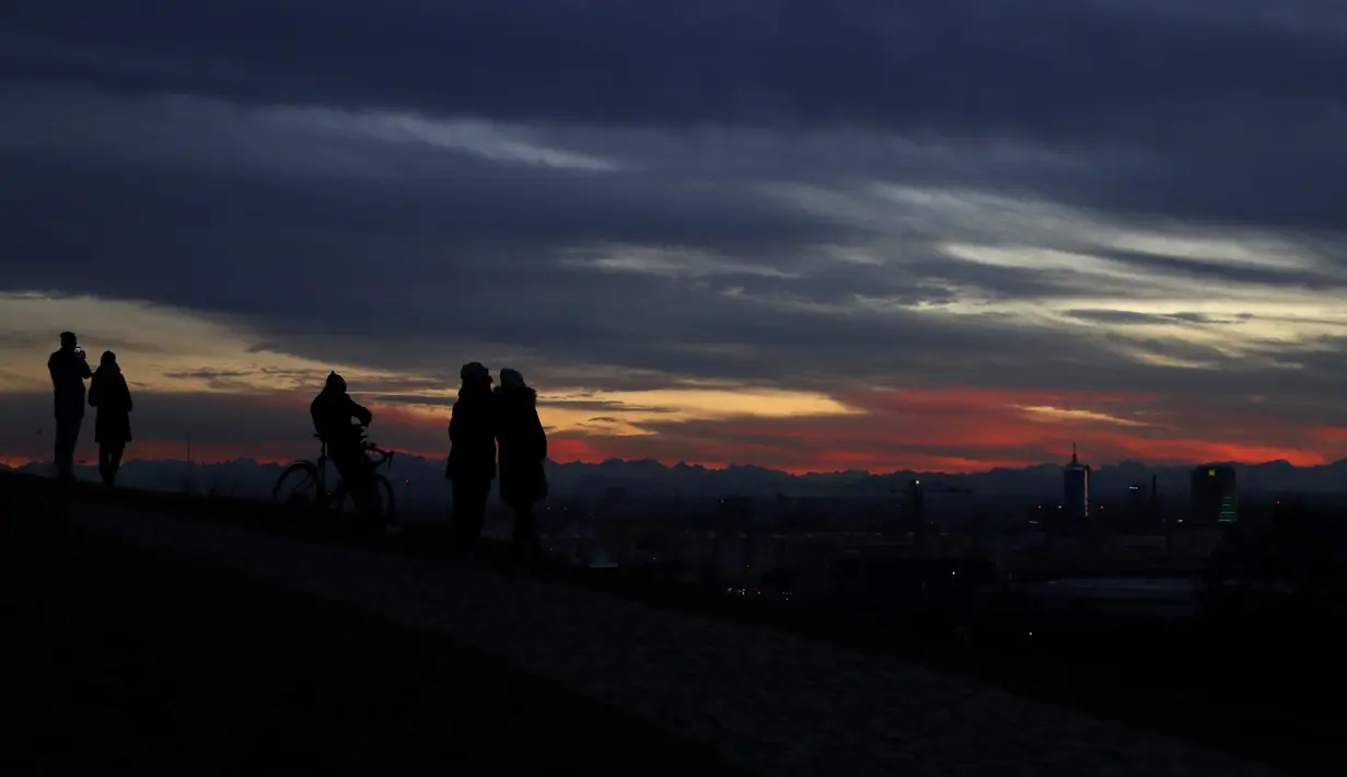 Orang-orang menyaksikan matahari terbenam di taman Olimpiade, Jerman (22/11/2020). Terletak di lingkungan Oberwiesenfeld Munich, Taman terus berfungsi sebagai tempat untuk acara budaya, sosial, dan agama, seperti acara ibadah. (AP Photo/Matthias Schrader)
