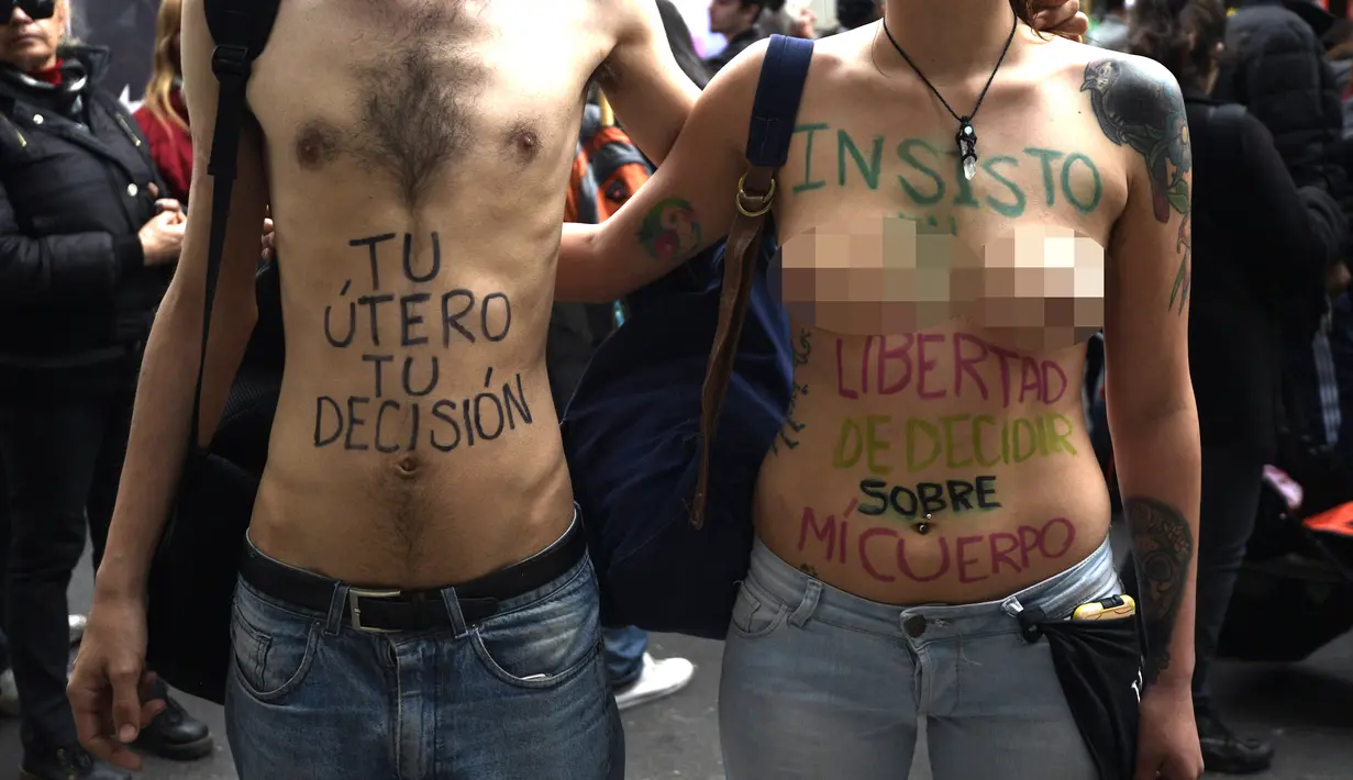 Sepasang demonstran bertelanjang dada saat menggelar aksi di Buenos Aires, Argentina (29/9). Dalam aksi ini badan mereka di cat dengan tulisan yang mengimbau bahwa rahim dan tubuh mereka kebebasan mereka. (AFP Photo/Juan Mabromata)