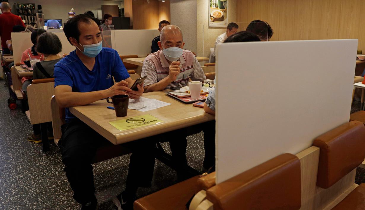 Orang-orang yang memakai masker menikmati makanan di restoran berpartisi di Hong Kong, Rabu (22/7/2020). Hong Kong telah mewajibkan penggunaan masker di semua area publik tertutup termasuk mal dan pasar seiring penambahan kasus baru harian Covid-19. (AP Photo/Kin Cheung)
