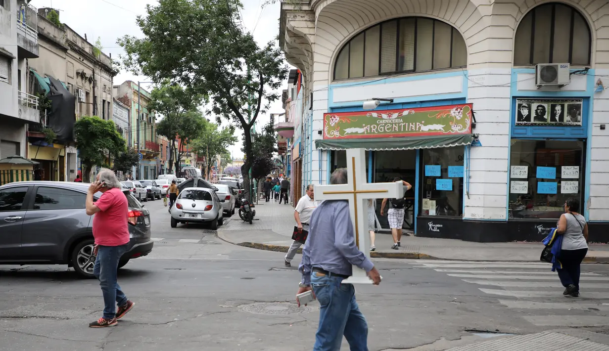 Seorang pria memegang salib berjalan di lingkungan La Boca, Buenos Aires pada 27 November 2018. La Boca berarti 'mulut', karena kedekatannya dengan sungai yang menjadikannya pelabuhan para imigran Eropa di masa lalu. (Ludovic MARIN / AFP)