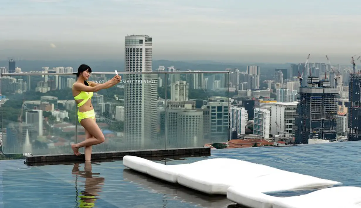 Seorang pengunjung wanita mengabadikan gambarnya saat di kolam renang dari atap Marina Bay Sands Singapura, Selasa (20/05/2014) (AFP PHOTO/Roslan Rahman)