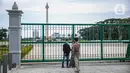 Warga berfoto di belakang Monumen Nasional atau Monas di Jakarta, Jumat (1/1/2021). Walaupun Monas ditutup warga tetap memanfaatkan libur Tahun Baru untuk berwisata dan berfoto di kawasan Monas. (Liputan6.com/Faizal Fanani)