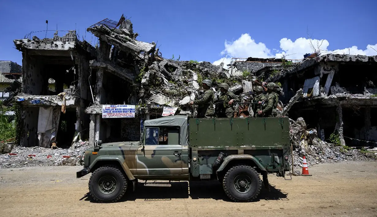 Tentara menaiki truk melewati bangunan yang hancur di Kota Marawi, Mindanao, Filipina, 23 Mei 2019. Kota yang sempat dikuasai ISIS tersebut tetap menjadi reruntuhan, para ahli pun memperingatkan bahwa upaya rekonstruksi yang macet memperkuat daya tarik kelompok ekstremis. (Noel CELIS/AFP)