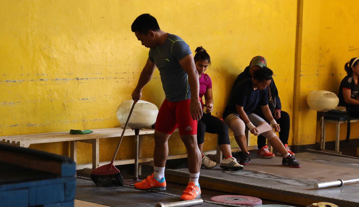 Eko Yuli membersihkan bantalan tempat berlatih dekat halaman Parkir Angkat Besi di Senayan, Jakarta, Senin (11/1/2016).  Hal ini karena tempat Latihan dalam tahap renovasi. (Bola.com/Nicklas Hanoatubun)