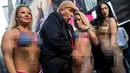 Seorang seniman berpenampilan seperti Donald Trump meraba-raba wanita seksi berbikini saat berada di depan Times Square di New York, (25/10). Aksi ini dilakukan oleh seniman Alison Jackson. (AFP Photo/Drew Angerer/Getty Images)
