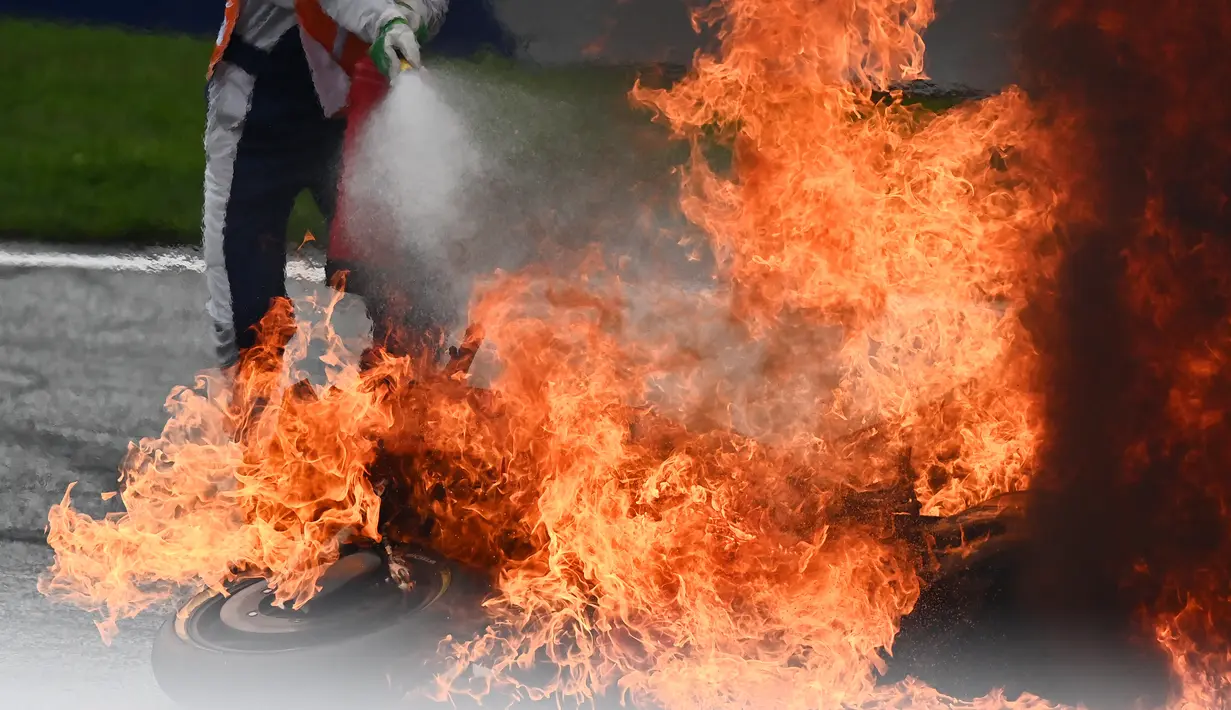 Seorang petugas trek mencoba memadamkan sepeda motor yang terbakar menyusul kecelakaan yang melibatkan pembalap Aprilia Gresini, Lorenzo Savadori dan pembalap KTM, Dani Pedrosa saat balapan MotoGP Styria 2021 di Red Bull Ring, Minggu (8/8/2021). (JOE KLAMAR/AFP)
