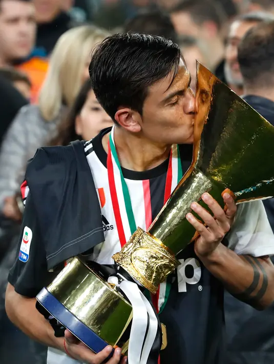 Striker Juventus, Paulo Dybala mencium Piala Liga Italia Serie A usai menjuarainya untuk ke-33 kalinya di Stadion Allianz, Turin (19/5/2019). Juventus berhasil mengunci titel juara Liga Italia 2018/2019. (AP Photo/Antonio Calanni)