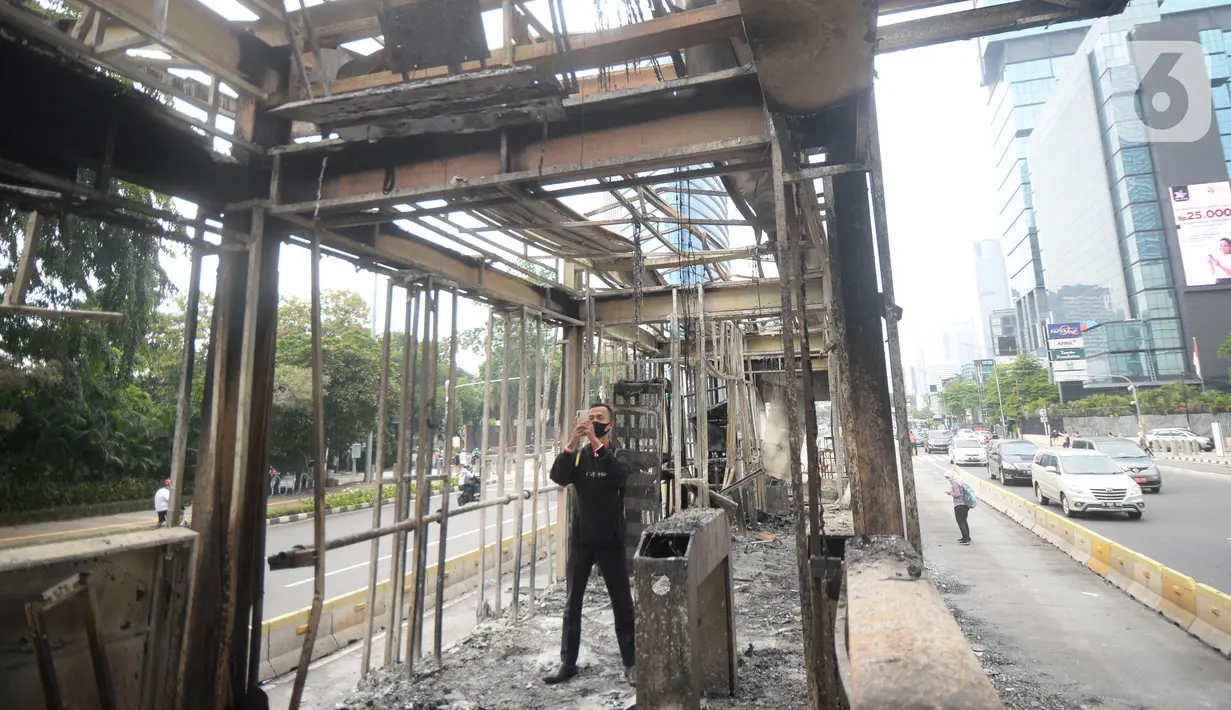 Seorang pria mengambil gambar halte transjakarta yang dibakar oleh massa perusuh di Kawasan Bundaran HI Jakarta, Jumat (9/10/2020). Demo menolak omnibus law Undang-Undang (UU) Cipta Kerja diwarnai kericuhan dan pembakaran terhadap sejumlah halte Transjakarta. (merdeka.com/Dwi Narwoko)