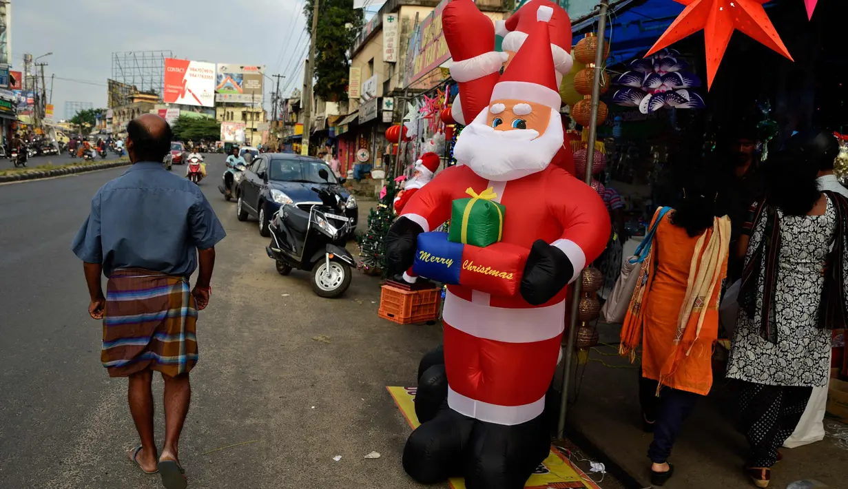 Warga berjalan melintasi balon Santa Claus dan barang hiasan Natal lainnya yang dipajang di toko pinggir jalan di Thiruvananthapuram, negara bagian Kerala, India, (19/12). Umat Kristen akan merayakan Hari Natal pada 25 Desember. (AP Photo / R S Iyer)