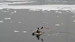 Seorang pria mendayung rakitnya sambil mengumpulkan bahan-bahan daur ulang dekat potongan busa tercemar yang mengambang di Sungai Yamuna, New Delhi, India, 26 Desember 2021. Sungai Yamuna tercemari limbah beracun dari industri. (Sajjad HUSSAIN/AFP)