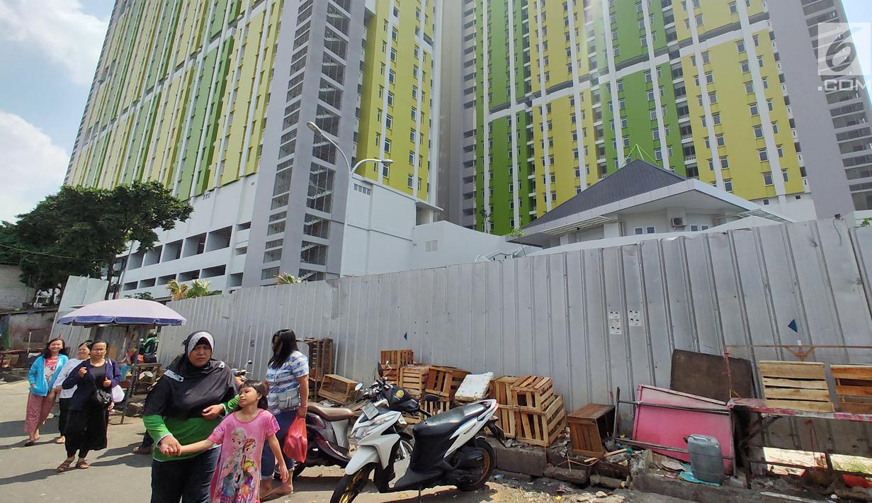 Warga berjalan dekat proyek Rusunawa Pasar Rumput yang hampir selesai pengerjaannya di Jakarta, Selasa (16/7/2019). Rusunawa Pasar Rumput akan diresmikan oleh Presiden Joko Widodo atau Jokowi pada Agustus mendatang. (Liputan6.com/Immanuel Antonius)